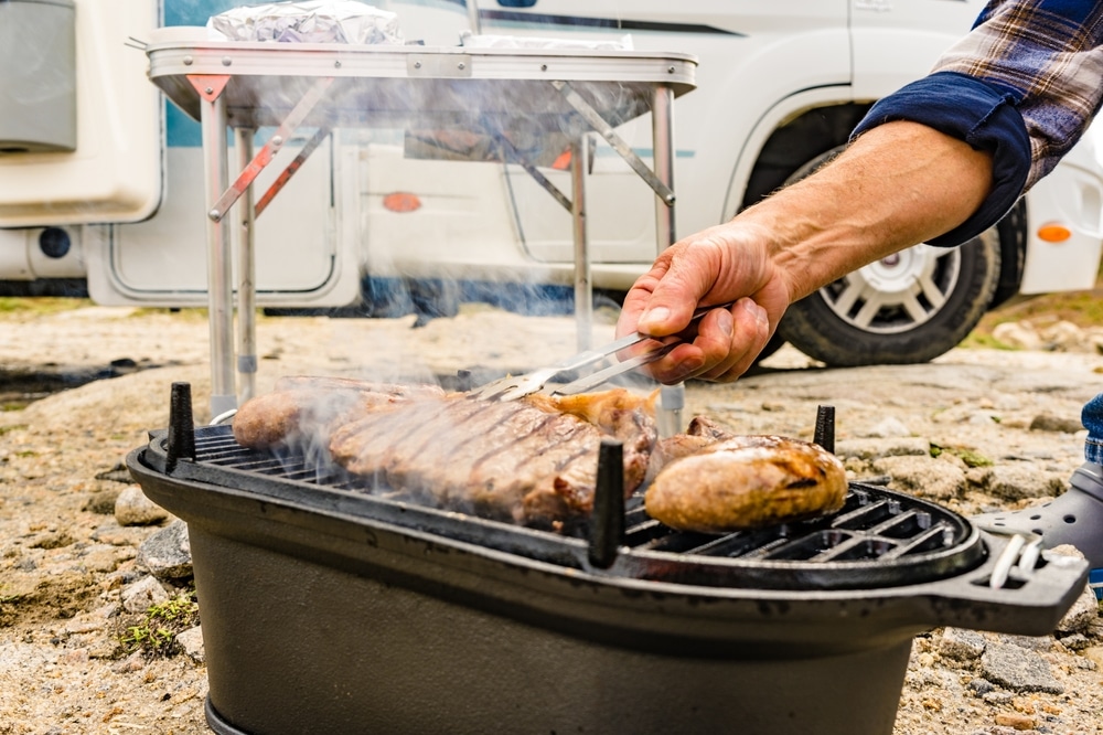 Man cooking on a barbecue in front of a caravan